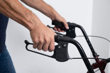 Hands gripping the ergonomic handles and loop brakes of a Nomad Rollator walker for mobility support.